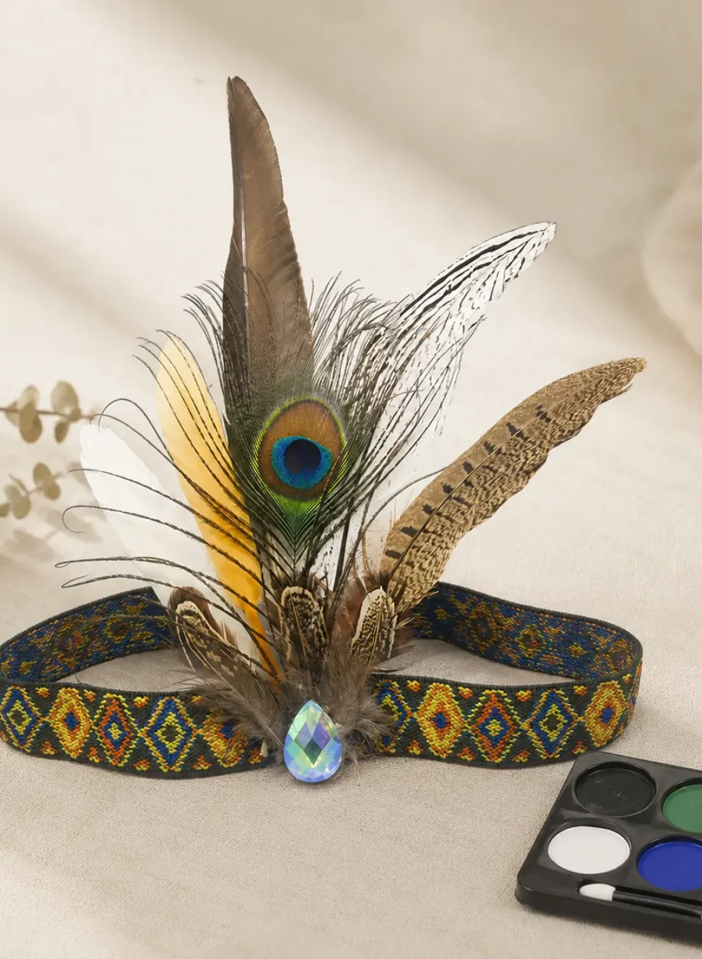 Aveline boho feather headband with natural feathers, a colorful woven band, crystal-style accent, and face paint palette.